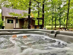 A hot tub in a forested area with a wooden cabin in the background. - Tranquil Lakefront Cabin Surrounded by Woods, Wildlife & Scenic Trails in  Williford, Arkansas (Williford)