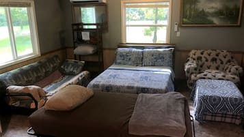 A cozy room with a bunk bed, a sofa, a chair, and a window with a view of greenery.
