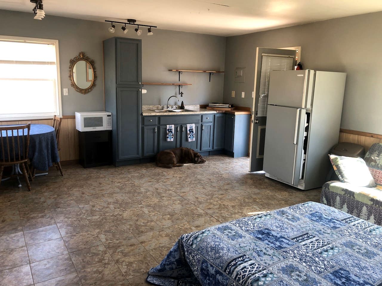 A compact kitchen with a microwave, sink, and refrigerator, a dining area with a table and chairs, and a sleeping area with a bed.