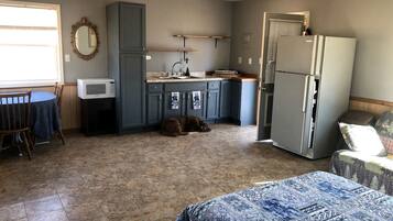 A compact kitchen with a microwave, sink, and refrigerator, a dining area with a table and chairs, and a sleeping area with a bed.
