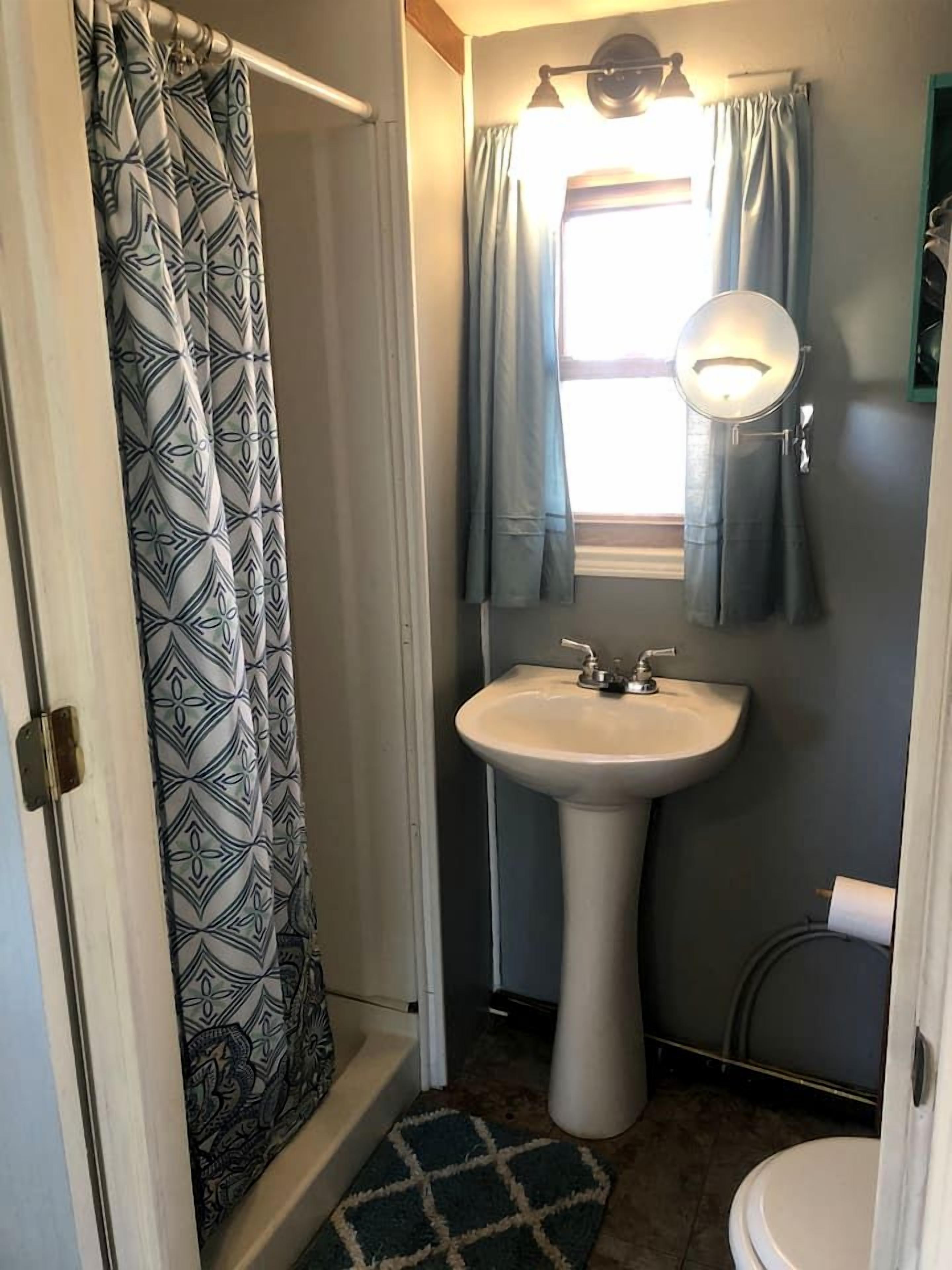 A bathroom with a shower curtain, a sink, a mirror, and a toilet.