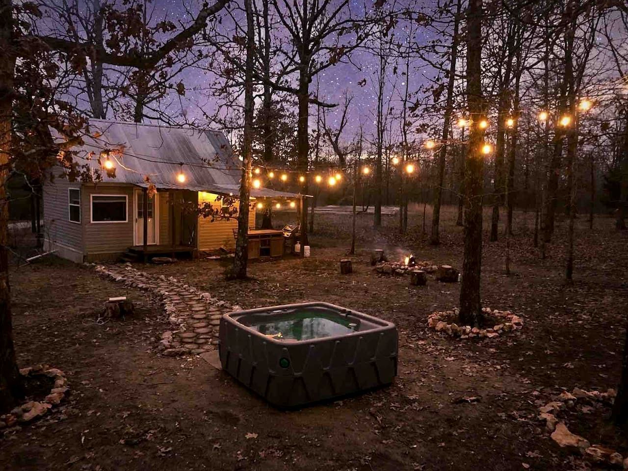 Una cabaña rústica con hidromasaje y luces colgantes en un área boscosa.