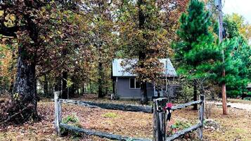 A rustic cabin surrounded by trees, a wooden fence, and a utility pole.