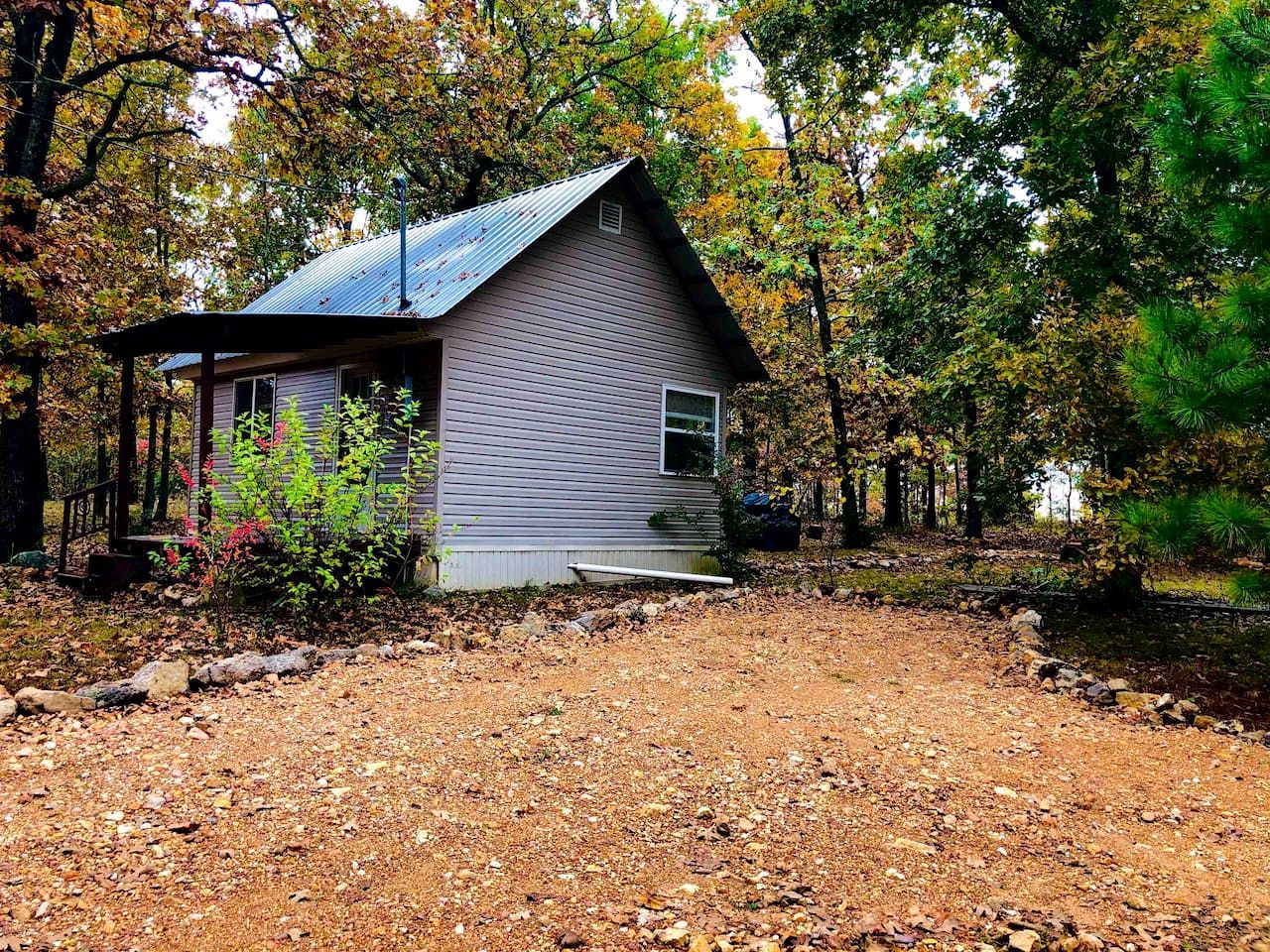 A small house with a metal roof, surrounded by trees and a gravel path.