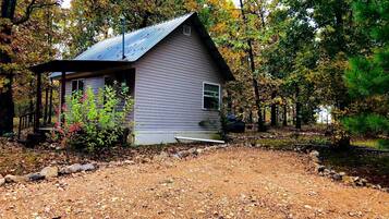 A small house with a metal roof, surrounded by trees and a gravel path.