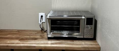 A microwave oven on a wooden shelf in a corner of a room.