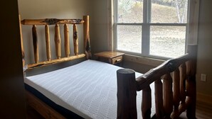 Ein Schlafzimmer mit hölzernem Kopfteil, einem Fenster mit Blick, einem Nachttisch und einem Bett mit gemustertem Überwurf.