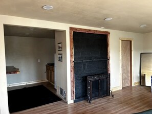 A room with a fireplace, wooden flooring, and a door leading to another room. - Spacious Cabin with Fire Pit, Perfect for a Family Getaway to Custer State Park (Sturgis)