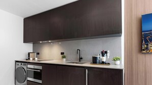 Une cuisine moderne avec des meubles de couleur sombre, des appareils électroménagers en acier inoxydable et un tableau représentant un paysage urbain accroché au mur.