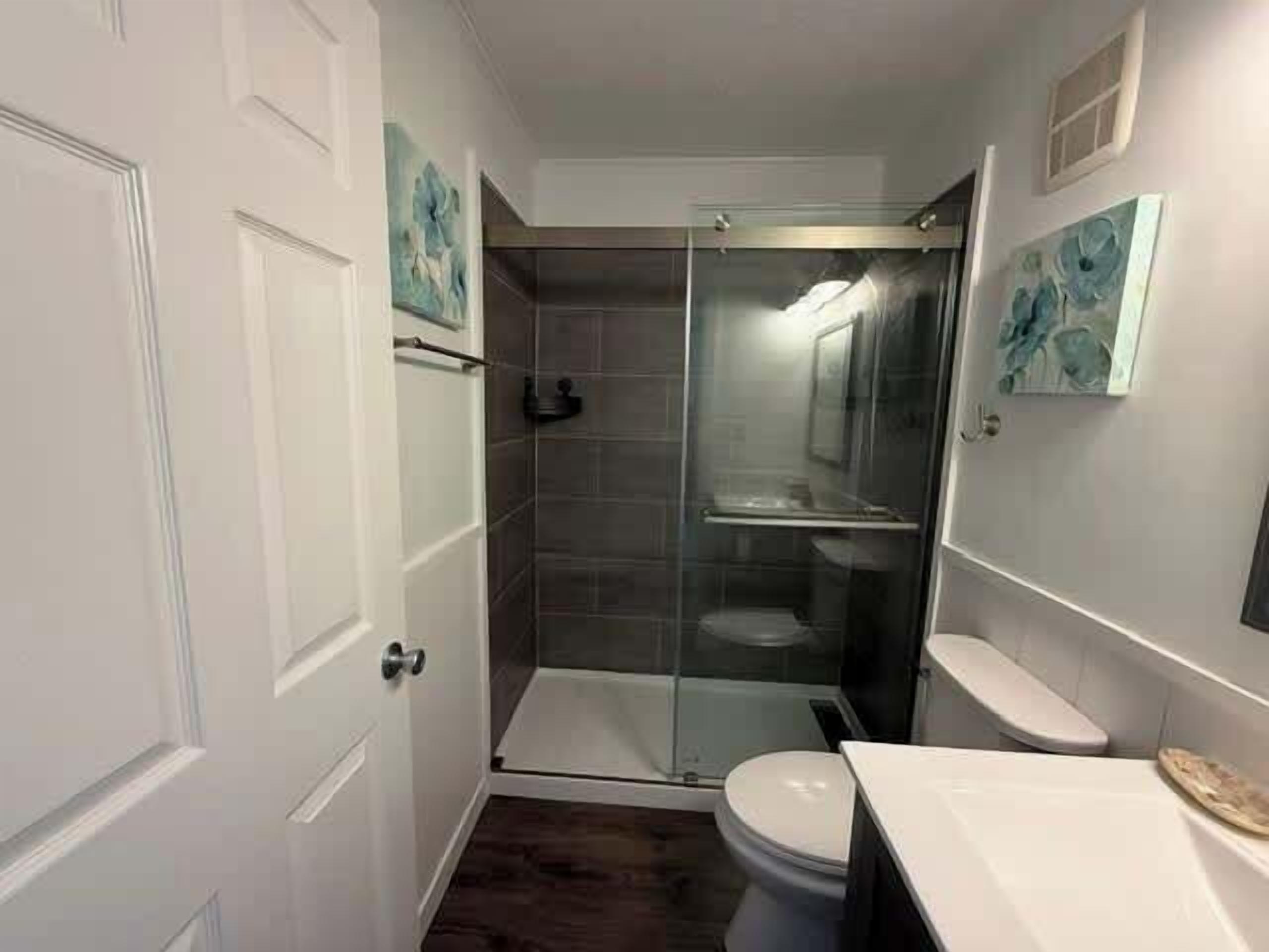A bathroom with a glass shower enclosure, a toilet, and a sink.