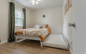 A bedroom with a bed, a window with curtains, a wall-mounted light, and a ceiling fan.