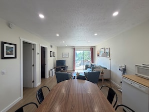 Un coin repas avec une table et des chaises en bois, un téléviseur et un canapé à l’arrière-plan.