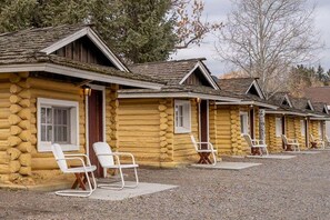 Une rangée de chalets en rondins, dotés d’un espace extérieur aménagé et d’une allée en gravier.