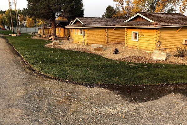 Une rangée de chalets en rondins, avec une pelouse bien entretenue et un chemin de gravier.