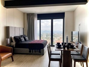 A modern hotel room with a large bed, a dining table with chairs, a TV, and a view of the city. - Studio in Anzures w/ Views, Gym & Jacuzzi (Ciudad de México)