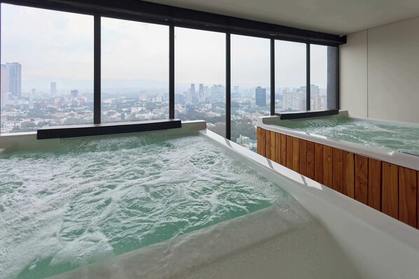 A high-rise hotel room with two hot tubs, large windows, and a cityscape view.