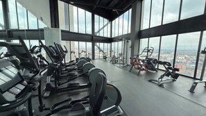 A gym with cardio machines and weight equipment, large windows with a city view.