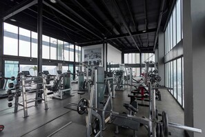 Ein Fitnessstudio mit unterschiedlichen Trainingsgeräten, großen Fenstern und einer hohen Decke.
