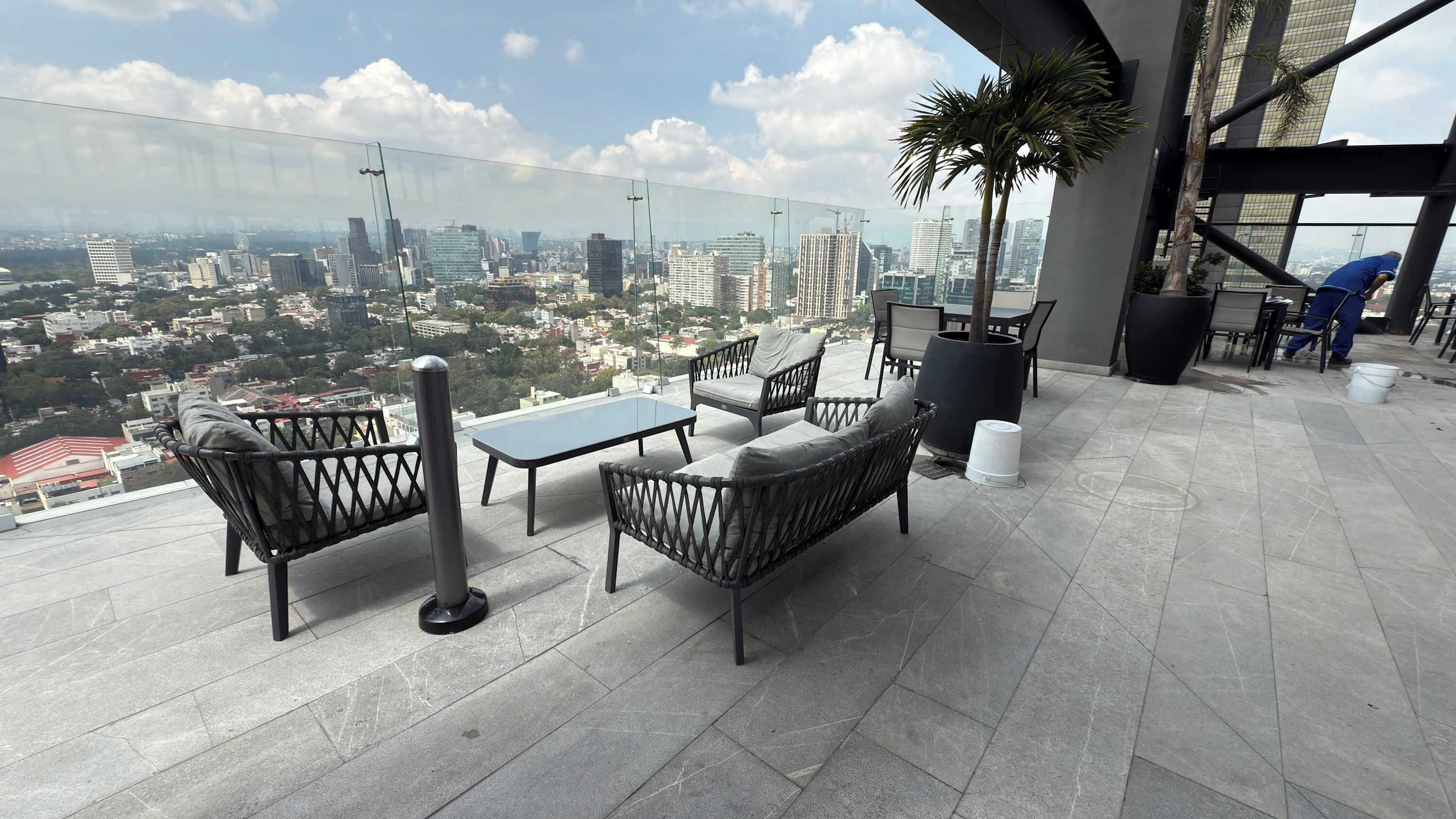 A rooftop terrace with a table and chairs, a potted plant, and a view of the cityscape.