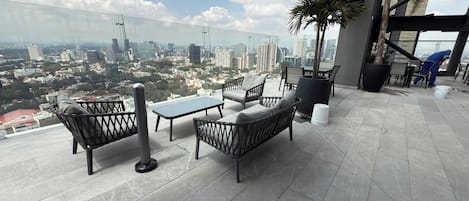 A rooftop terrace with a table and chairs, a potted plant, and a view of the cityscape.