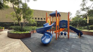 Ein Spielplatz mit Rutschen und Klettergerüsten, umgeben von Pflanzkästen und Bäumen.
