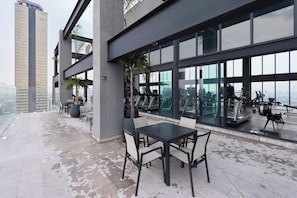 Eine Dachterrasse mit Glasfassade, Sitzgelegenheiten im Freien und Fitnessgeräten.