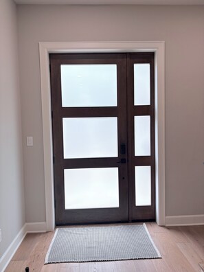 Une porte dotée de panneaux en verre dépoli, un bouton de porte et un paillasson devant l’entrée.