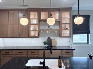 Une cuisine avec des meubles de rangement en bois, un plan de travail noir, un évier et des luminaires suspendus.