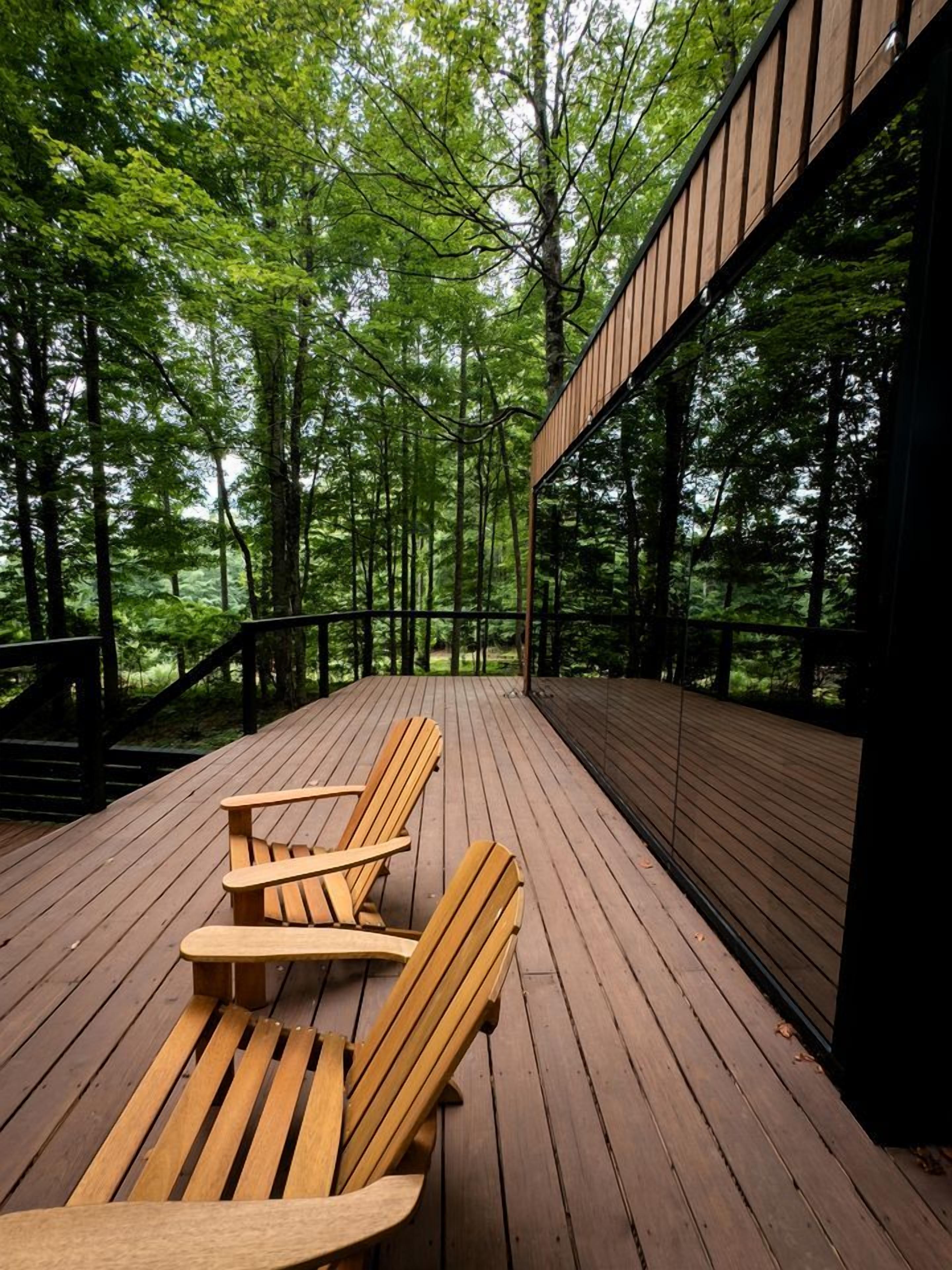 A wooden deck with chairs, surrounded by trees.