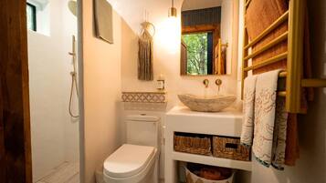 A compact bathroom with a toilet, a sink with a stone basin, a mirror, and a towel rack.