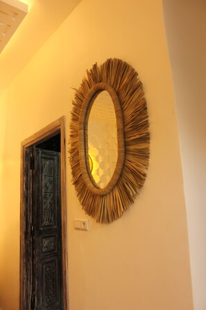 A room with a wooden door, a textured wall, and a circular mirror with a fringe design. - Riad tumsilt (Marrakech)