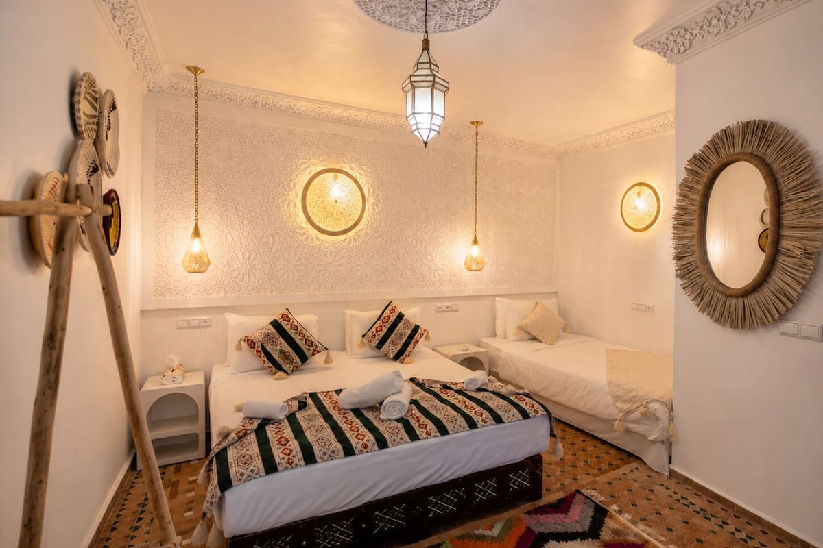 A room with a bed, two bedside tables, a hanging light fixture, a mirror, and a patterned rug.