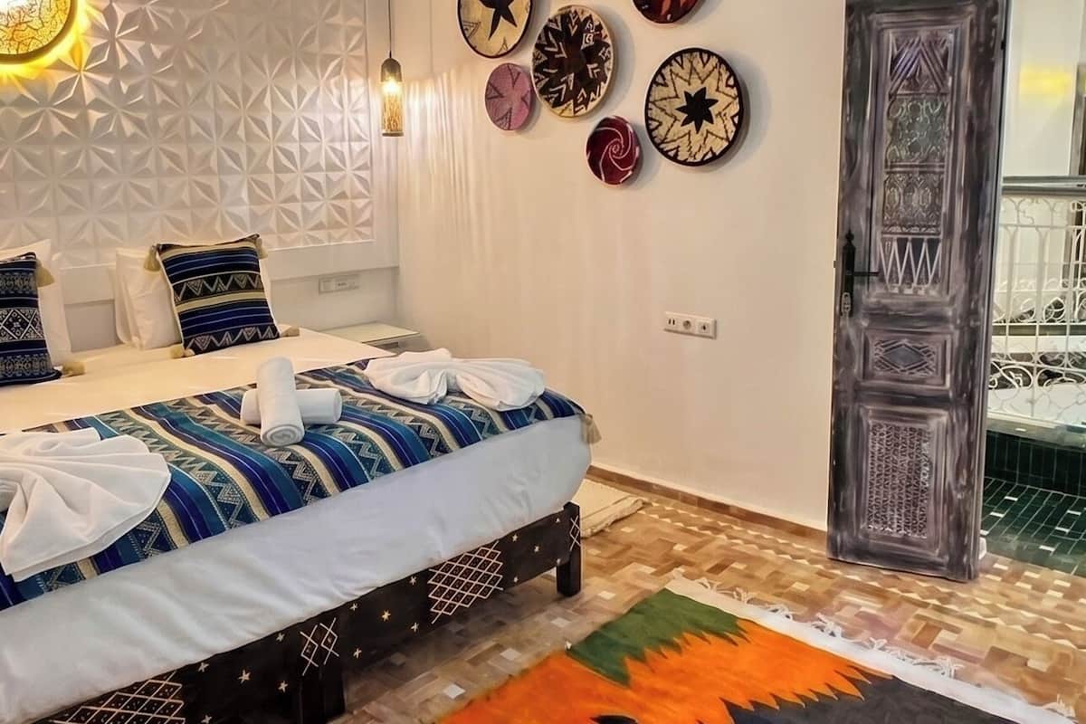 A bedroom with a patterned ceiling, a bed with a geometric-patterned bedspread, a wall-mounted clock, and a decorative door.
