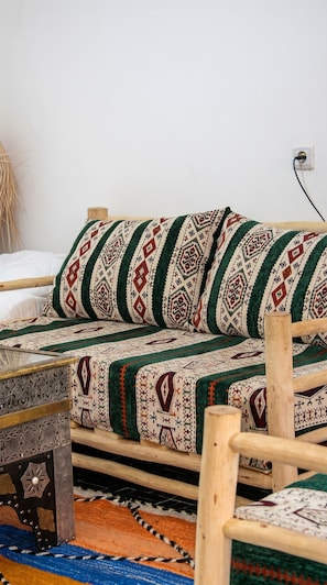 A traditional woven sofa with a patterned cover, a wooden side table, and a colorful rug. - Riad tumsilt (Marrakech)