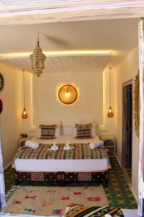 A bedroom with a bed, hanging light fixtures, and a wall-mounted light. - Riad tumsilt (Marrakech)