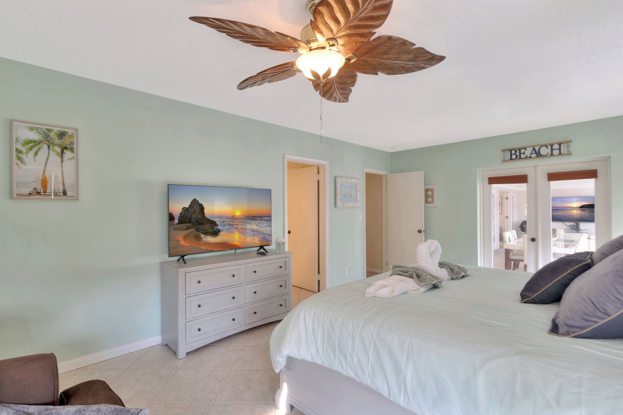 Un dormitorio con cama, ventilador de techo, cómoda y un cuadro de un atardecer.
