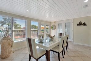 A dining area with a glass-top table, four chairs, a large vase, and a view of the outside. - Casa by The Cove 3BR 2BA plus Office (Deerfield Beach)