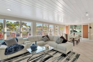 A modern living room with a sectional sofa, a glass coffee table, and a dining area with a table and chairs. - Casa by The Cove 3BR 2BA plus Office (Deerfield Beach)