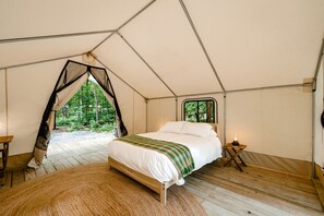 Ein Zelt mit Bett, Fenster und Blick auf den Wald.