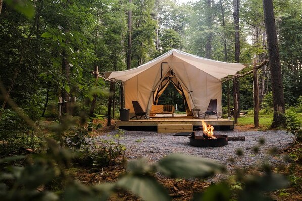 A tent with a fire pit and seating area in a forest.