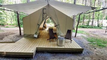 A tent with a wooden deck, a metal trash can, and a chair.