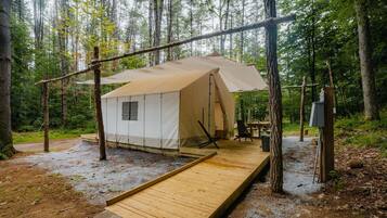 A tent with a wooden deck, a table, and chairs in a forest setting.