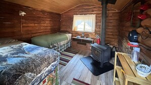 Una cabaña con interior de madera, una cama, un sofá, una chimenea y un ventanal con cortinas.
