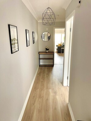A hallway with wooden flooring, a geometric pendant light, and framed artwork on the walls. - Luxury By The Coast 9 (Galway)