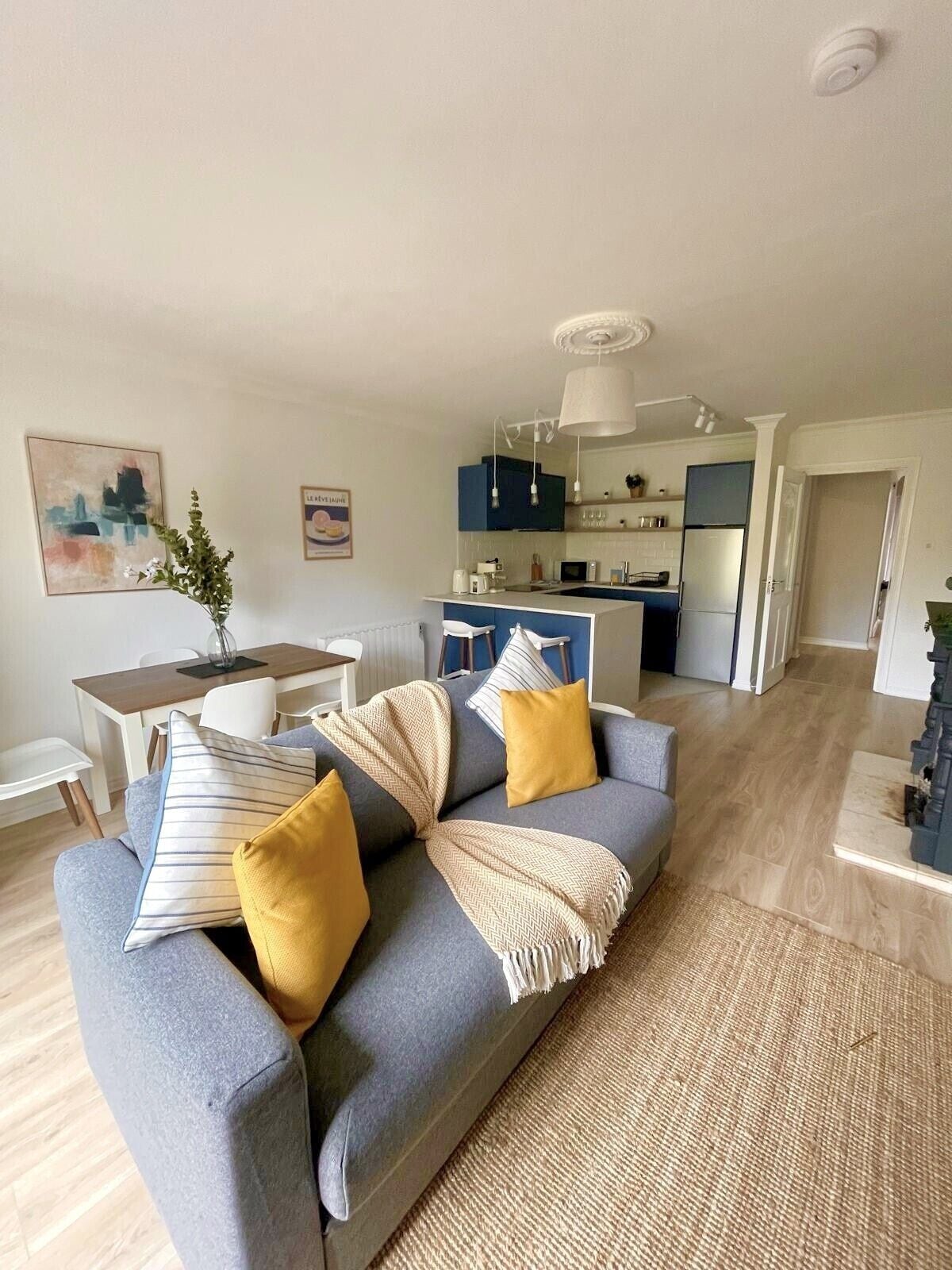 A modern living room with a grey sofa, yellow cushions, a woven rug, and a dining area with a table and chairs.