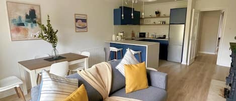 A modern living room with a grey sofa, yellow cushions, a woven rug, and a dining area with a table and chairs.