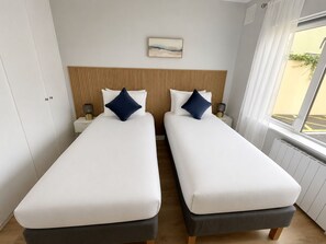 Une chambre double avec deux lits, une tête de lit en bois, une table de chevet avec une lampe et une fenêtre donnant sur un beau paysage.