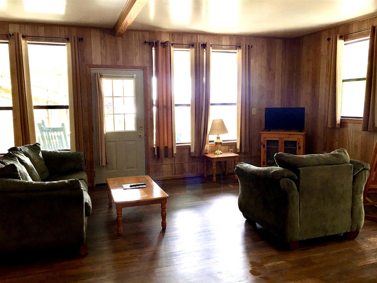 A room with wooden walls, a green sofa, a wooden coffee table, and a television on a cabinet.