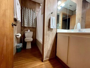 A narrow bathroom with a wooden floor, a toilet, a shower curtain, and a mirror above the sink. - Spacious Triplex Cabin with Lake View & Fishing Pier, Shared Outdoor Deck, Near Zwolle, LA (Zwolle)