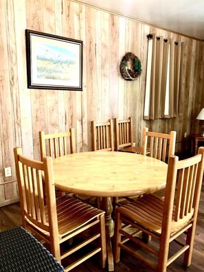 Une table à manger en bois, entourée de six chaises, un tableau encadré accroché au mur et une guirlande au-dessus des rideaux.